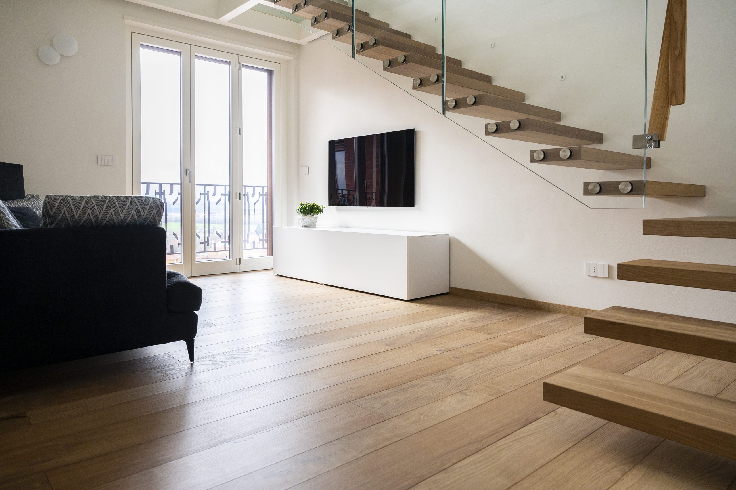 Ettore, pavimento e scala in rovere bio in un ambiente moderno con corrimano in vetro.