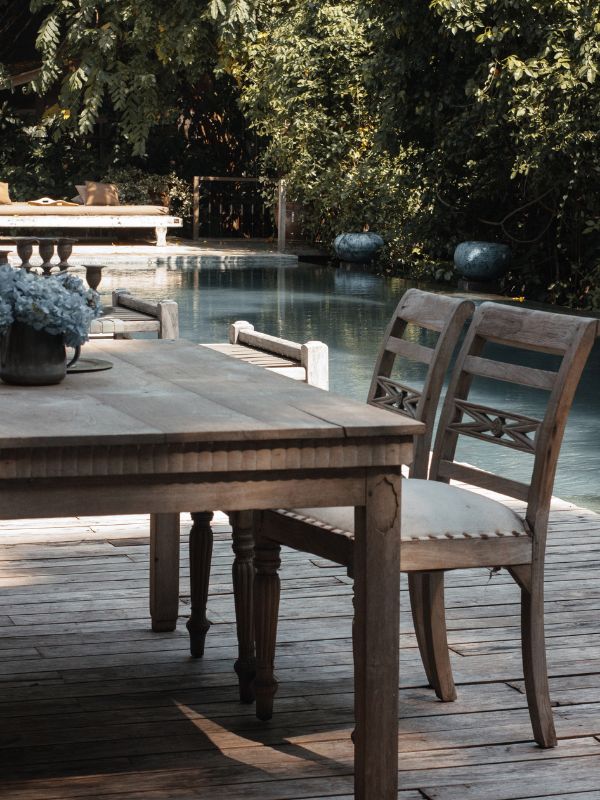 Area relax a bordo piscina con pavimentazione in decking e tavolo con sedie.